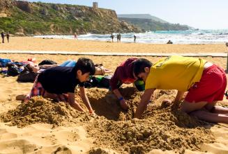 Chef de groupe et étudiants faisant un trou dans le sable à la plage